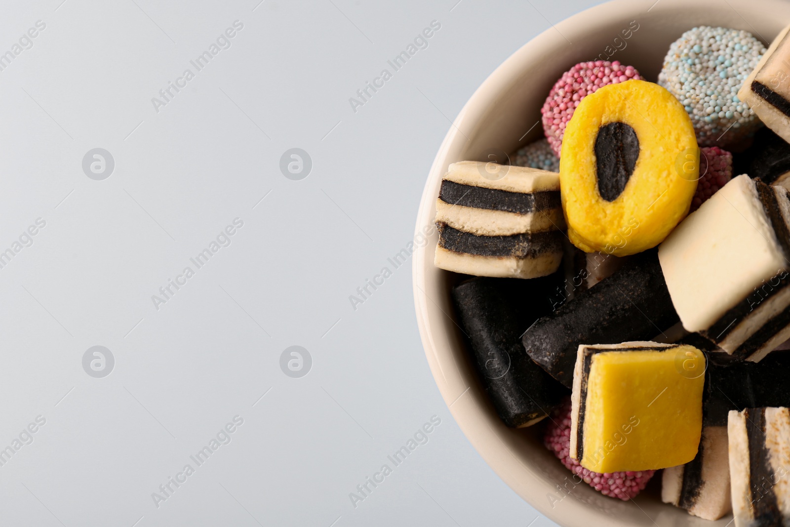 Photo of Bowl of tasty liquorice candies on light blue background, top view. Space for text