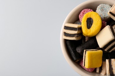 Bowl of tasty liquorice candies on light blue background, top view. Space for text