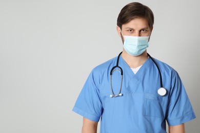Photo of Doctor or medical assistant (male nurse) with protective mask and stethoscope on light grey background. Space for text
