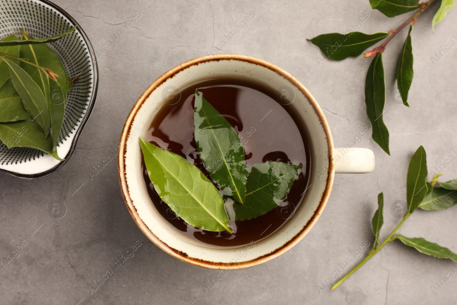 Photo of Cup of freshly brewed tea with bay leaves on grey table, flat lay