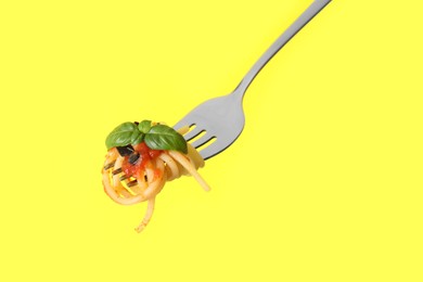 Photo of Fork with tasty pasta, basil and sauce on yellow background