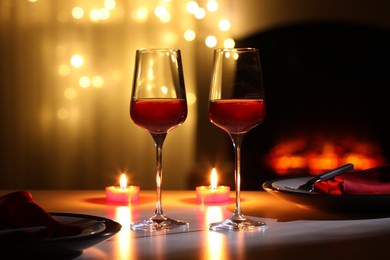 Photo of Glasses of wine and candles on table against blurred lights. Romantic dinner