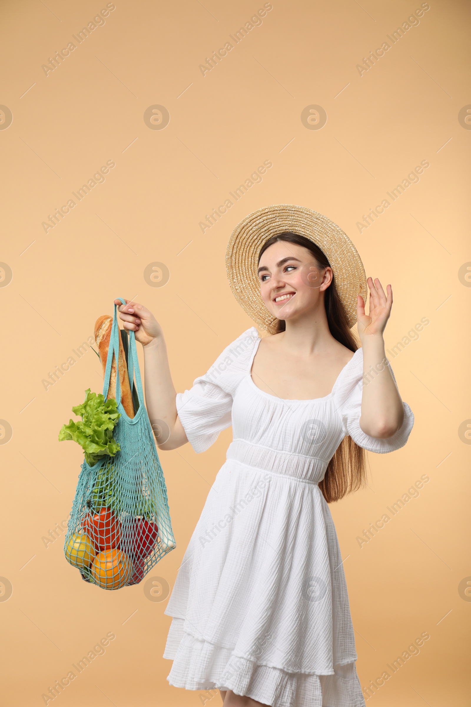 Photo of Woman with string bag of fresh vegetables and baguette on beige background, space for text