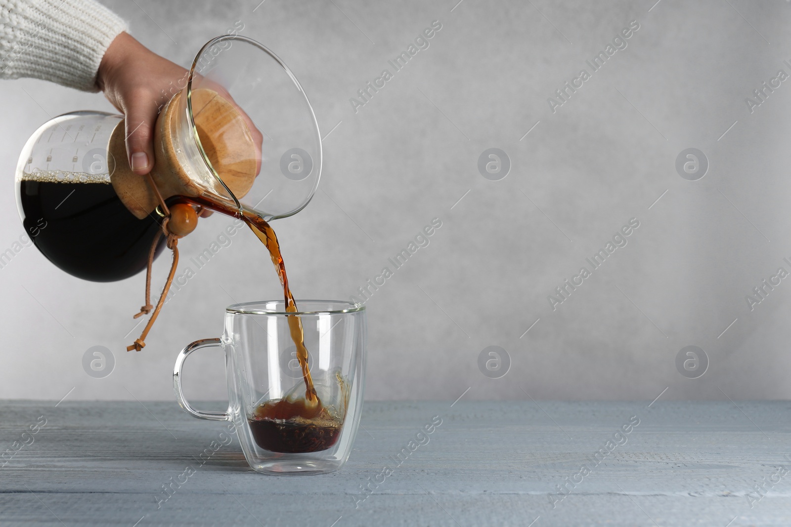 Photo of Woman pouring tasty drip coffee into cup at grey wooden table, closeup. Space for text