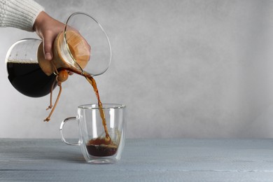 Photo of Woman pouring tasty drip coffee into cup at grey wooden table, closeup. Space for text