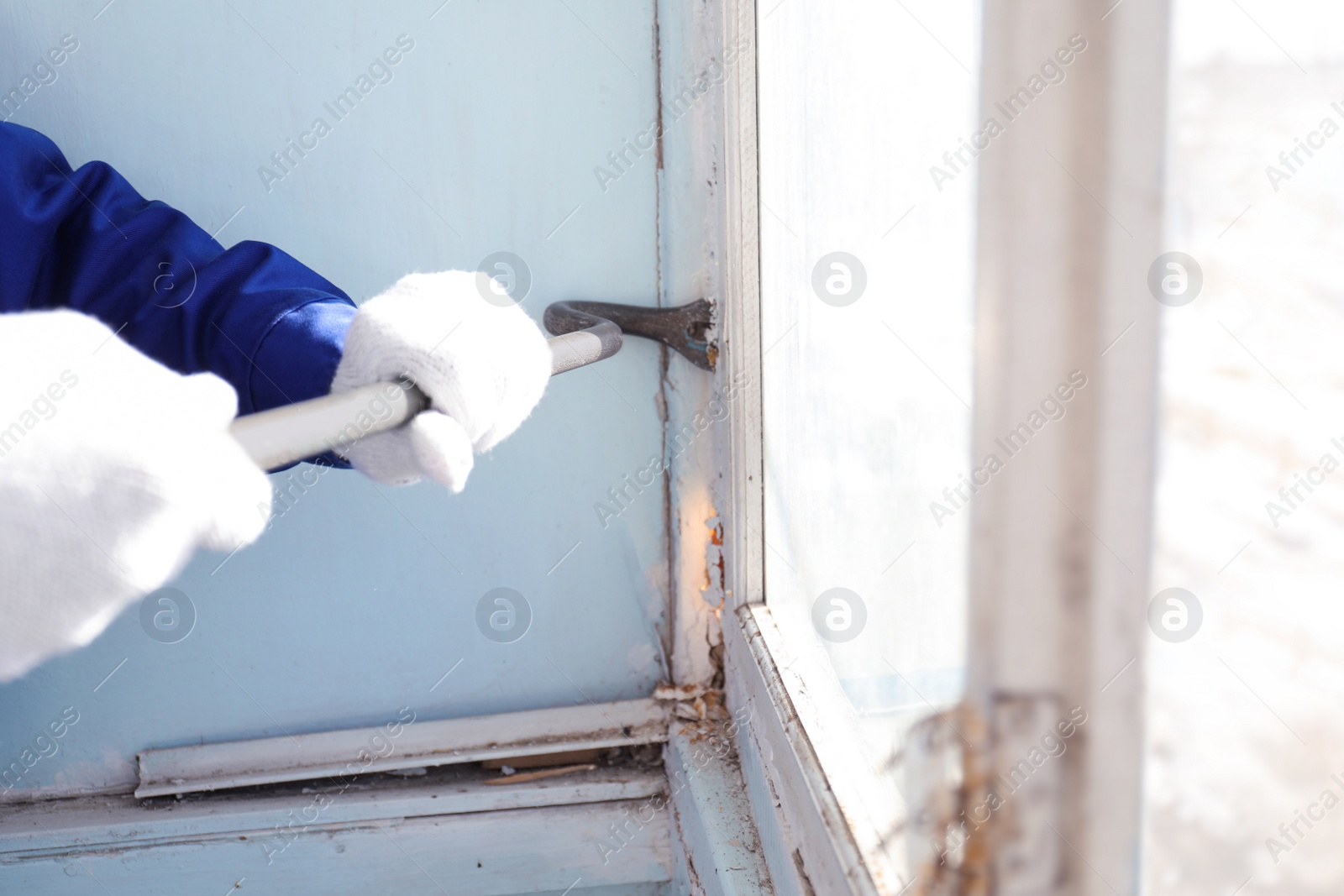 Photo of Worker dismantling old window with crowbar indoors, closeup