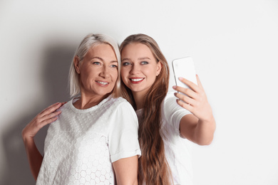 Happy mother and daughter taking selfie on white background
