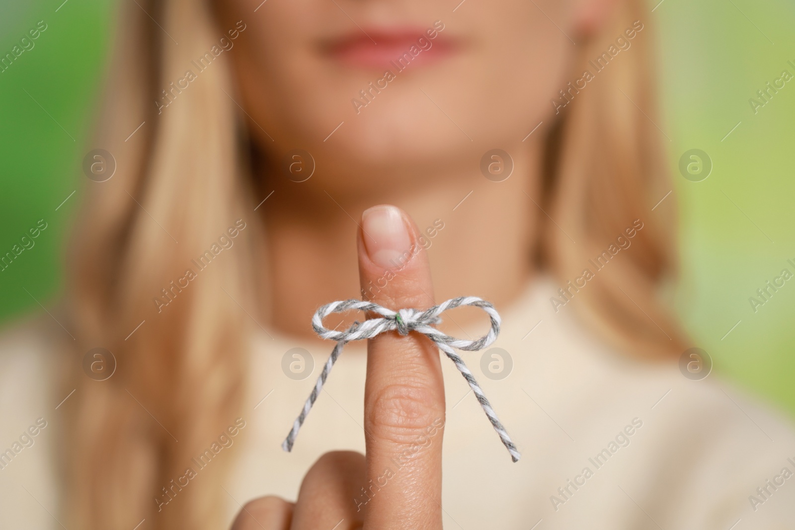 Photo of Woman showing index finger with tied bow as reminder against green blurred background, focus on hand