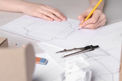 Woman creating packaging design at light wooden table, closeup