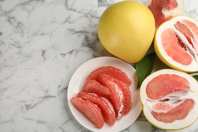 Photo of Fresh cut and whole pomelo fruits on white marble table, flat lay. Space for text