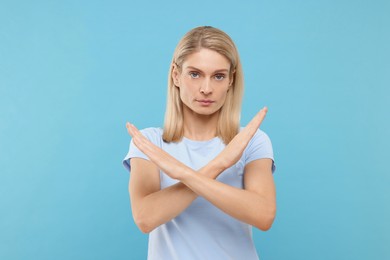 Photo of Stop gesture. Woman with crossed hands on light blue background