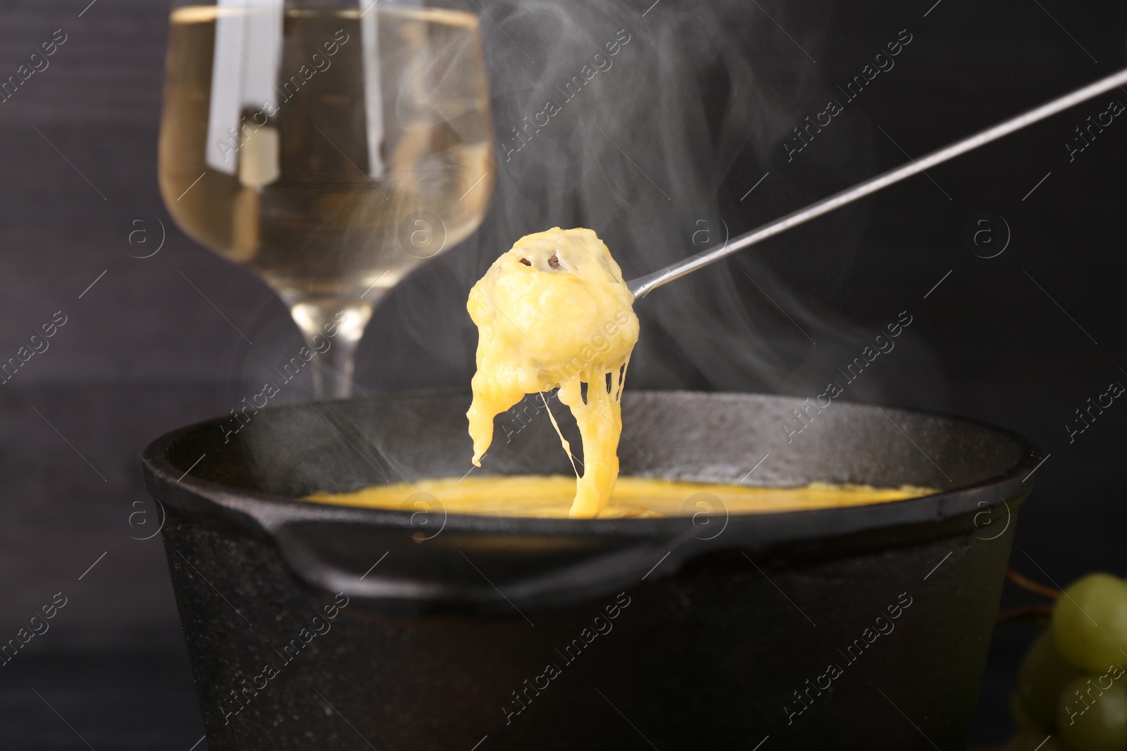 Image of Dipping piece of bread into fondue pot with tasty melted cheese at table, closeup