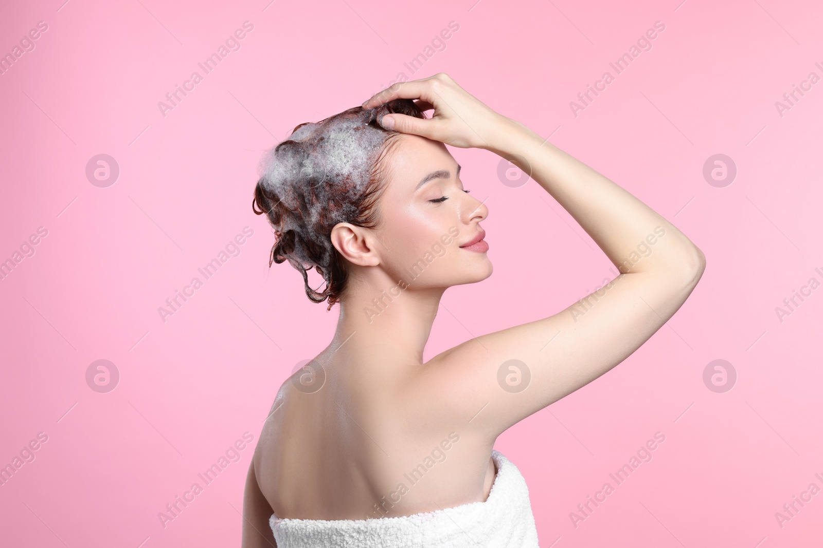 Photo of Happy young woman washing her hair with shampoo on pink background