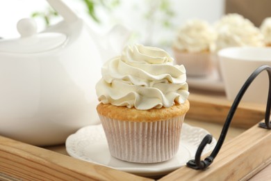 Tasty cupcake with vanilla cream and teapot on wooden tray, closeup