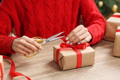 Photo of Woman decorating Christmas gift box at wooden table indoors, closeup