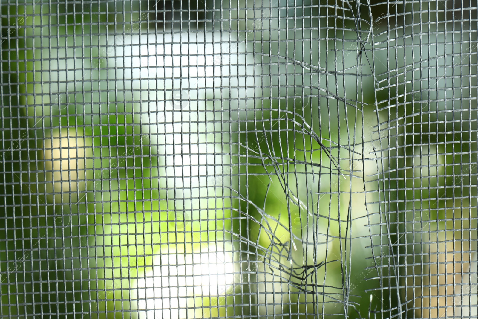 Photo of Torn window screen against blurred background, closeup