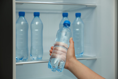 Woman with bottle of fresh water near open fridge, closeup