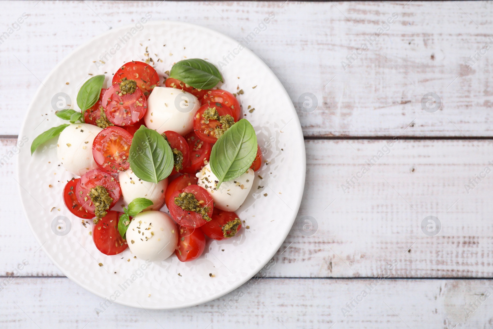Photo of Tasty salad Caprese with tomatoes, mozzarella balls and basil on white wooden table, top view. Space for text