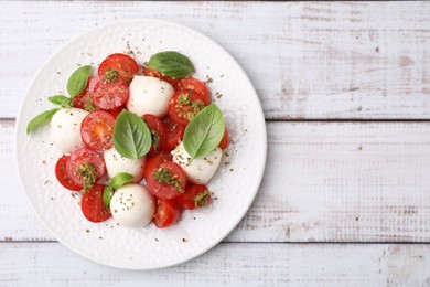 Photo of Tasty salad Caprese with tomatoes, mozzarella balls and basil on white wooden table, top view. Space for text