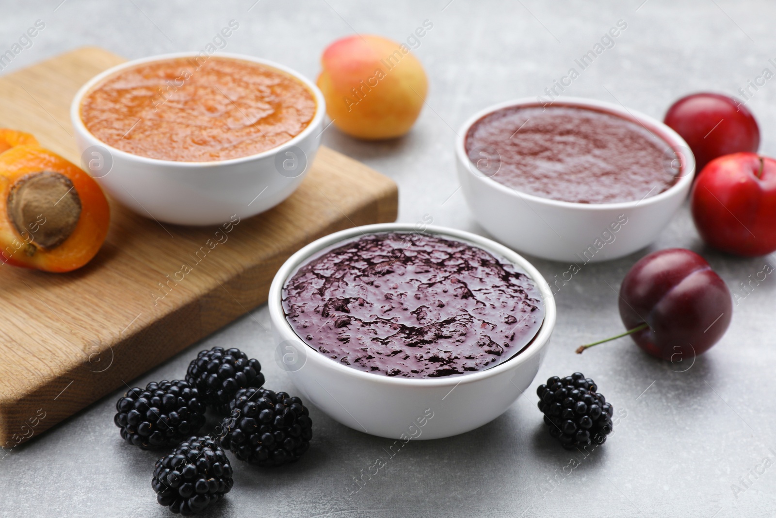 Photo of Different puree in bowls and fresh fruits on light grey table