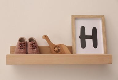 Wooden shelf with baby booties, toy and frame in room. Interior design