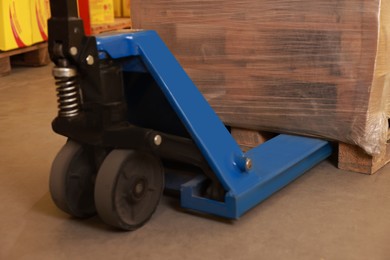 Wooden pallets wrapped in stretch on manual forklift indoors, closeup