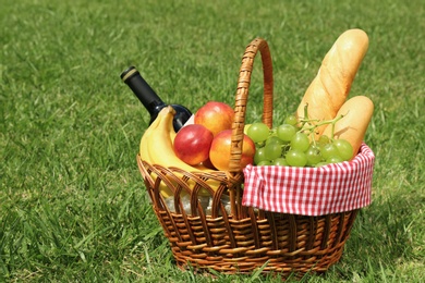 Photo of Basket with food and bottle of wine on lawn in park. Summer picnic