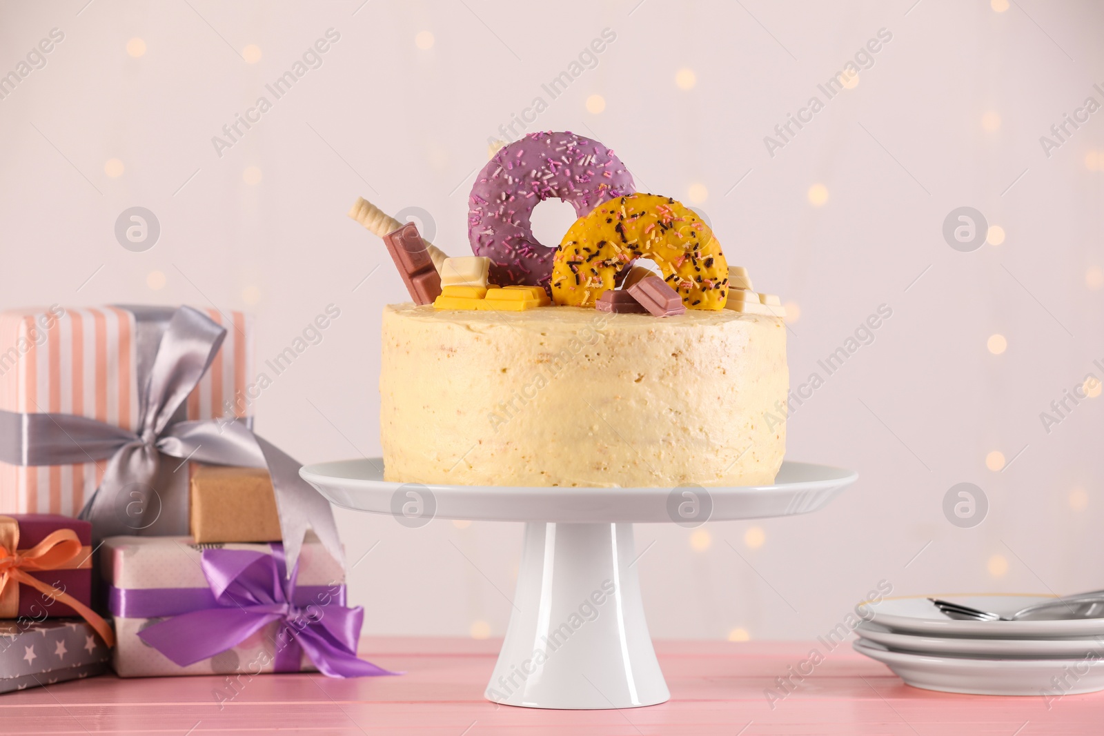 Photo of Delicious cake decorated with sweets, gift boxes, saucers and spoons on pink wooden table