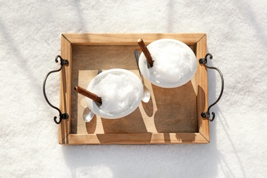 Tray with bowls of tasty ice cream and waffle rolls on snow, top view