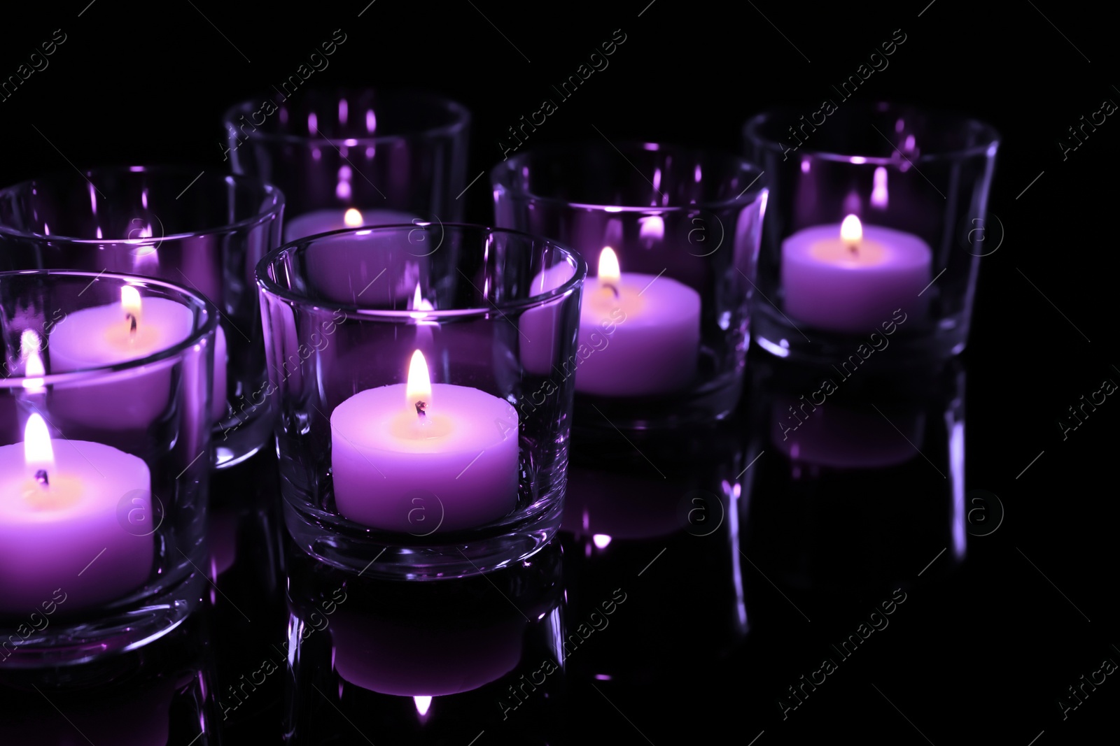 Image of Beautiful burning violet candles on black background, closeup. Funeral attributes