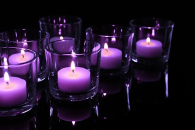 Image of Beautiful burning violet candles on black background, closeup. Funeral attributes