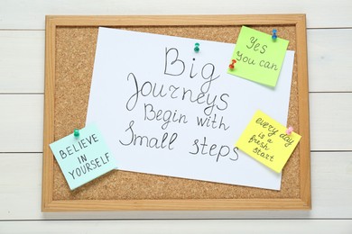 Photo of Corkboard with motivational quotes on white wooden table, top view