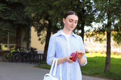 Young woman holding purse with banknotes outdoors