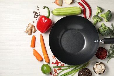 Photo of Empty iron wok surrounded by raw ingredients on white wooden table, flat lay. Space for text