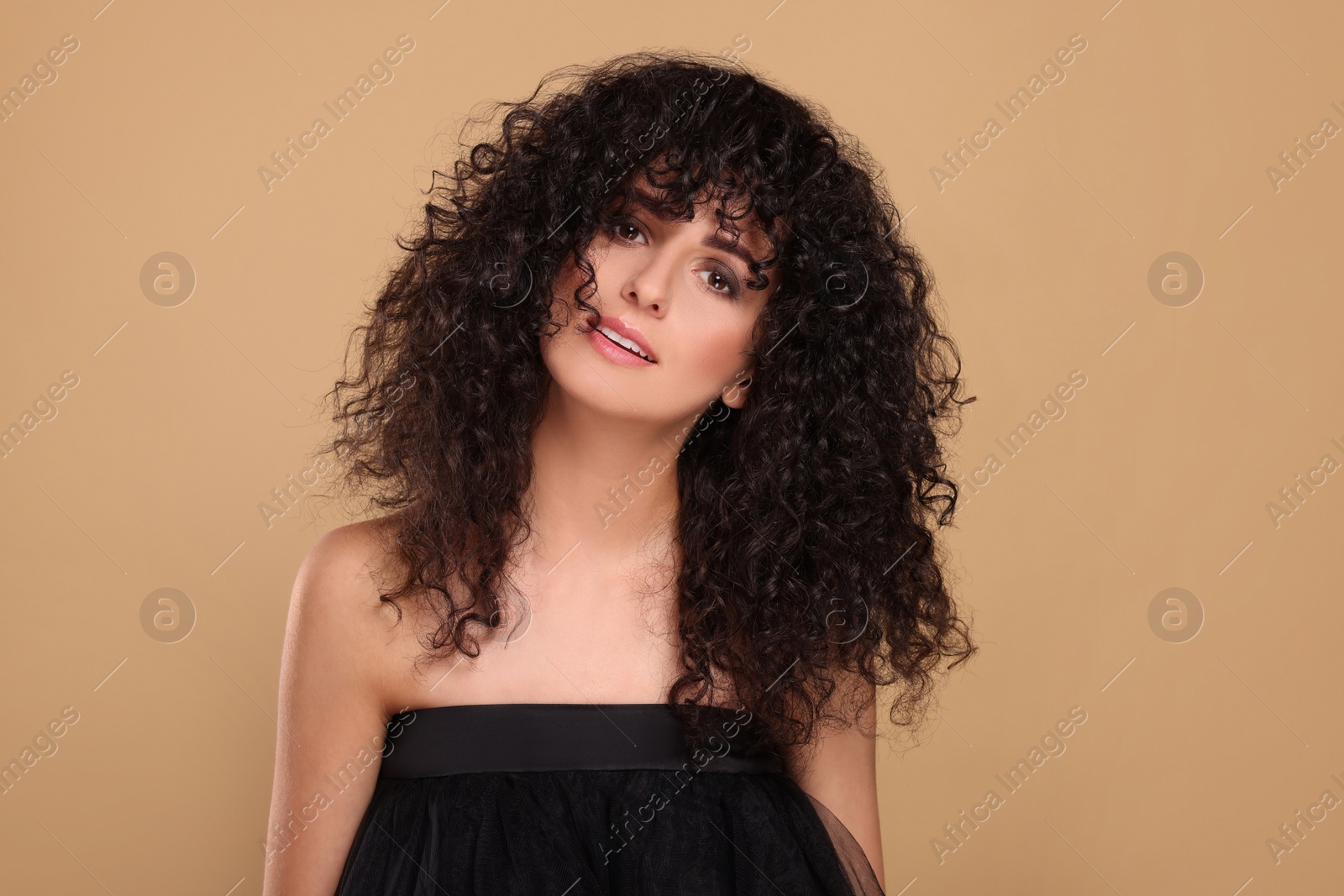 Photo of Beautiful young woman with long curly hair on beige background