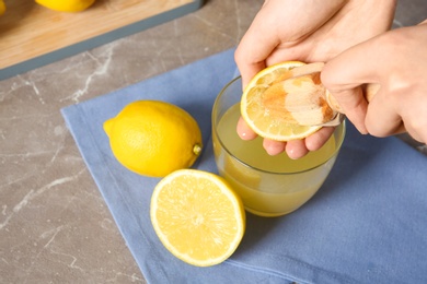 Photo of Woman squeezing lemon juice with reamer into glass on table