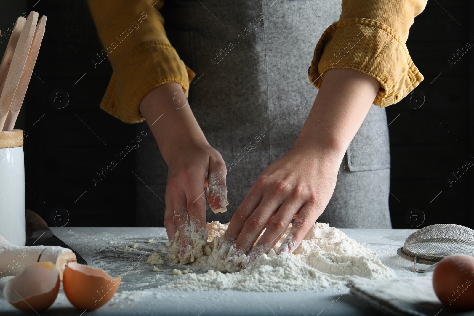 Photo of Woman kneading dough at table on black background, closeup