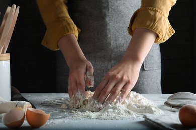 Photo of Woman kneading dough at table on black background, closeup