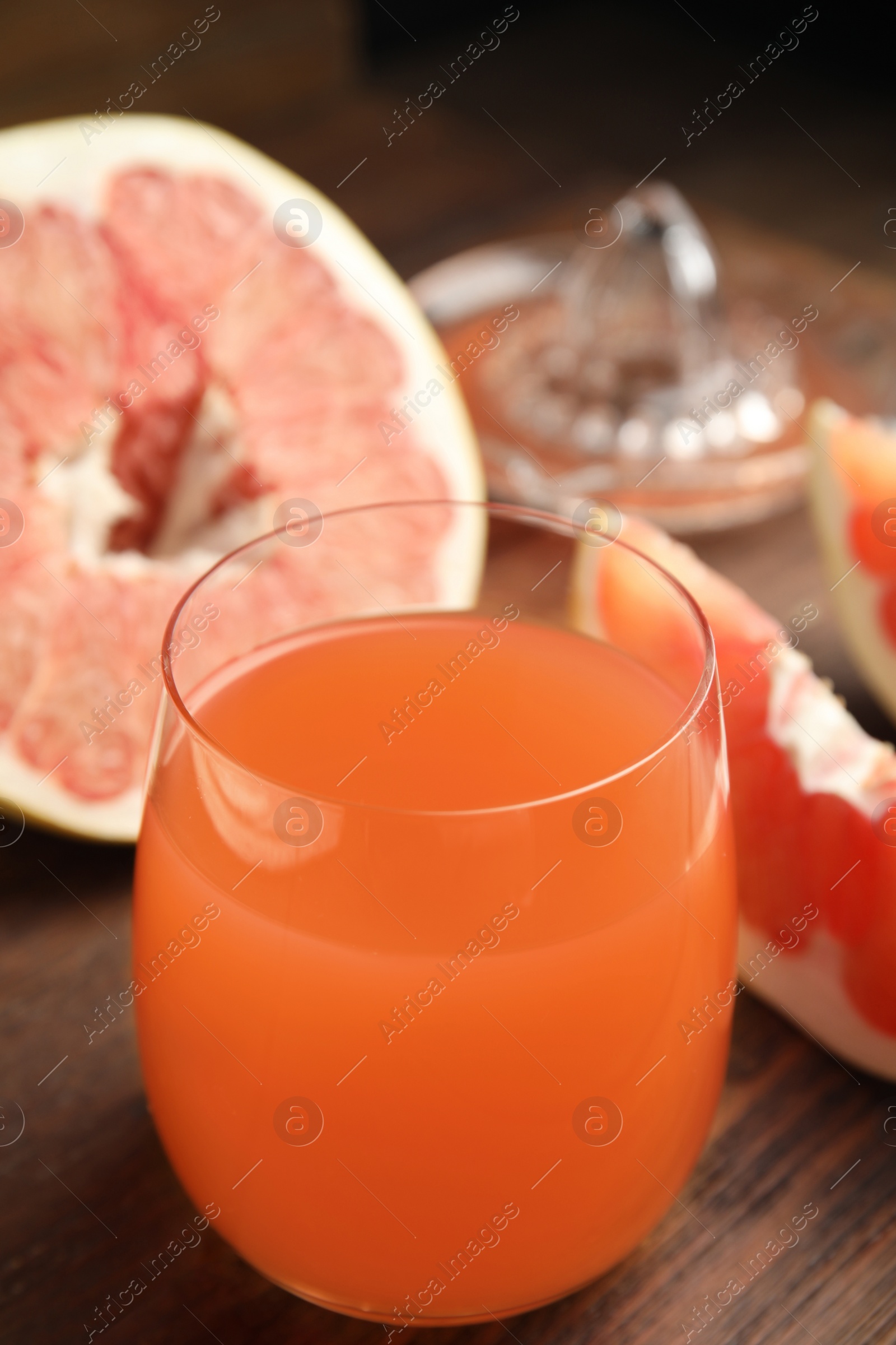 Photo of Glass of pink pomelo juice and fruit on wooden table, closeup