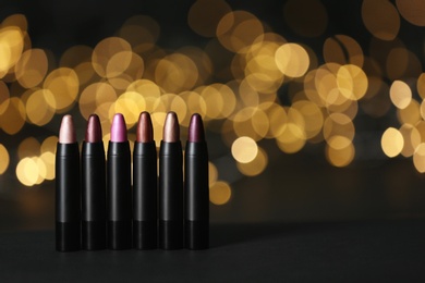 Photo of Set of bright lipsticks on table against blurred lights, space for text