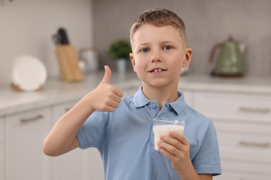 Cute boy with glass of fresh milk showing thumb up in kitchen