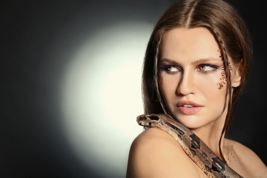 Photo of Beautiful woman with boa constrictor on dark background. Space for text