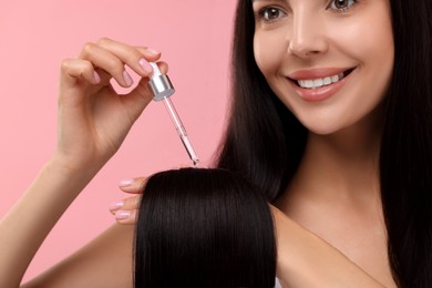 Photo of Beautiful woman applying hair serum on pink background, closeup. Cosmetic product