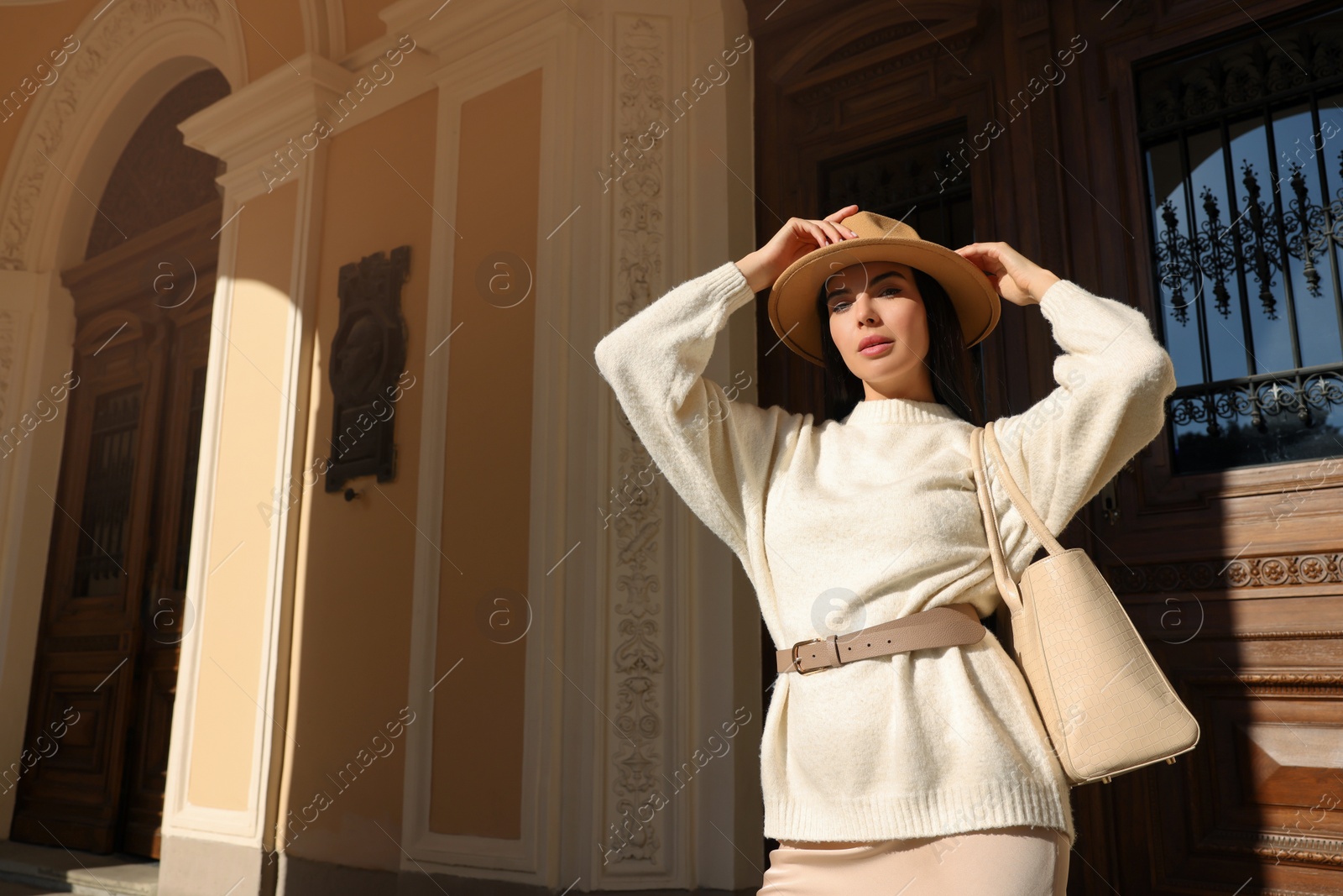 Photo of Young woman with stylish bag outside beautiful building, low angle view. Space for text