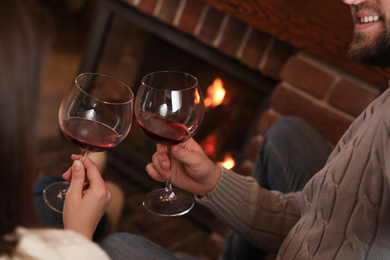 Photo of Lovely couple with glasses of wine resting near fireplace at home, closeup. Winter vacation