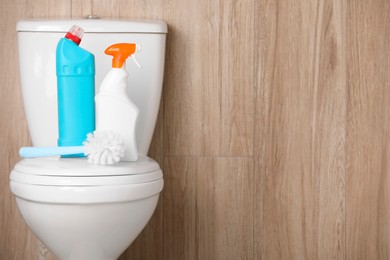 Photo of Bottles of cleaning products and brush on toilet bowl indoors, space for text