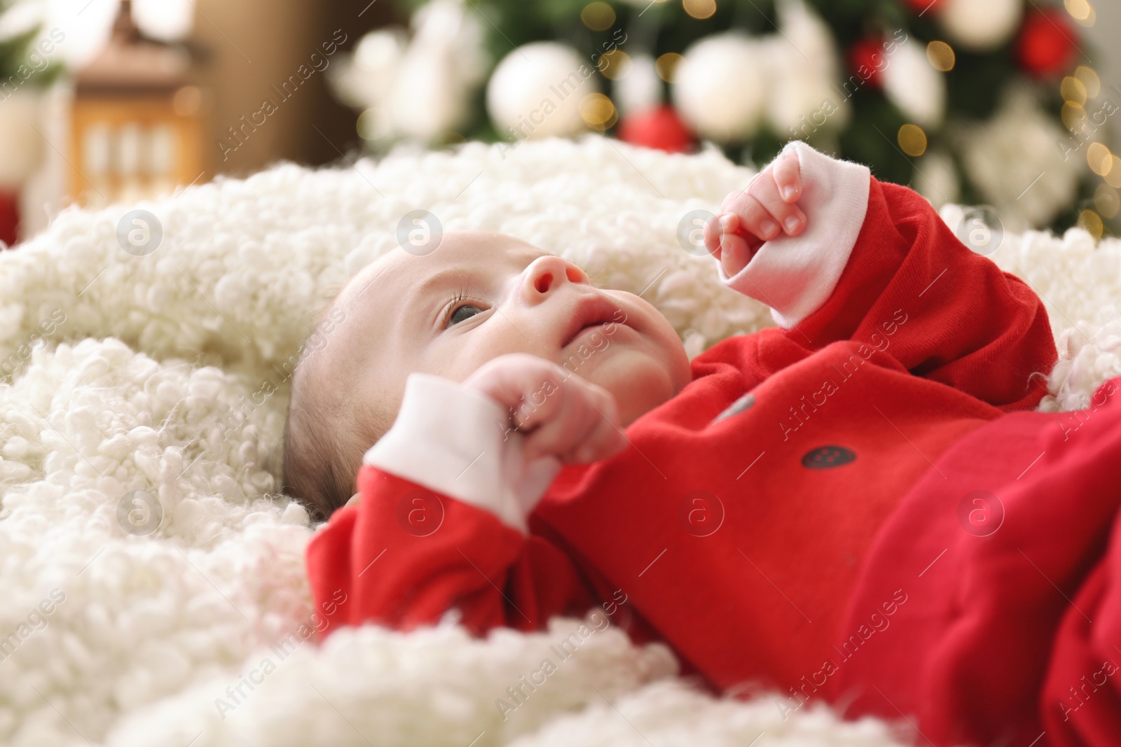 Photo of Cute little baby on soft blanket in room decorated for Christmas, closeup