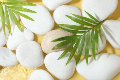 Photo of Spa stones and palm leaves in water on yellow background, flat lay