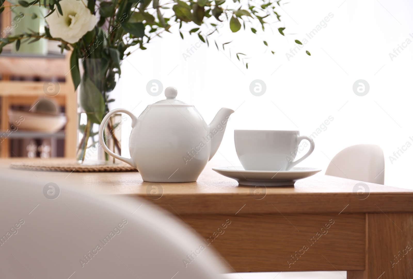 Photo of Teapot, cup and flowers on wooden dining table indoors. Kitchen interior