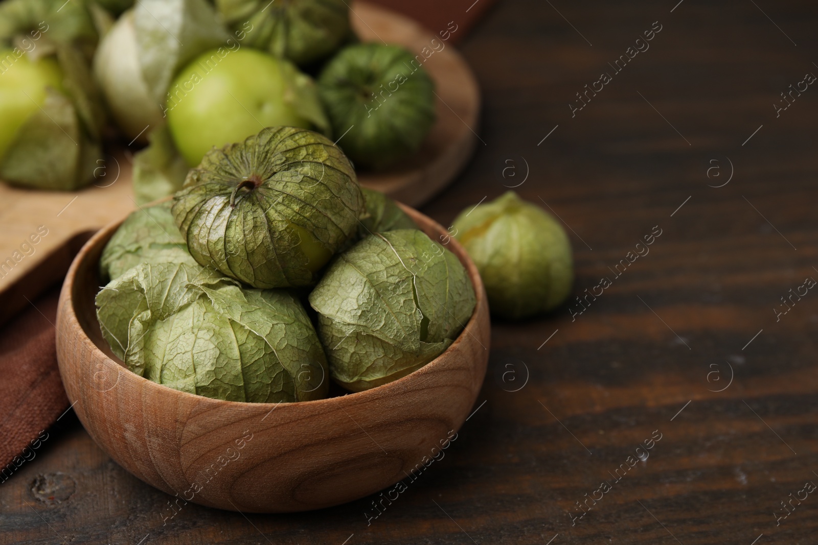 Photo of Fresh green tomatillos with husk in bowl on wooden table, closeup